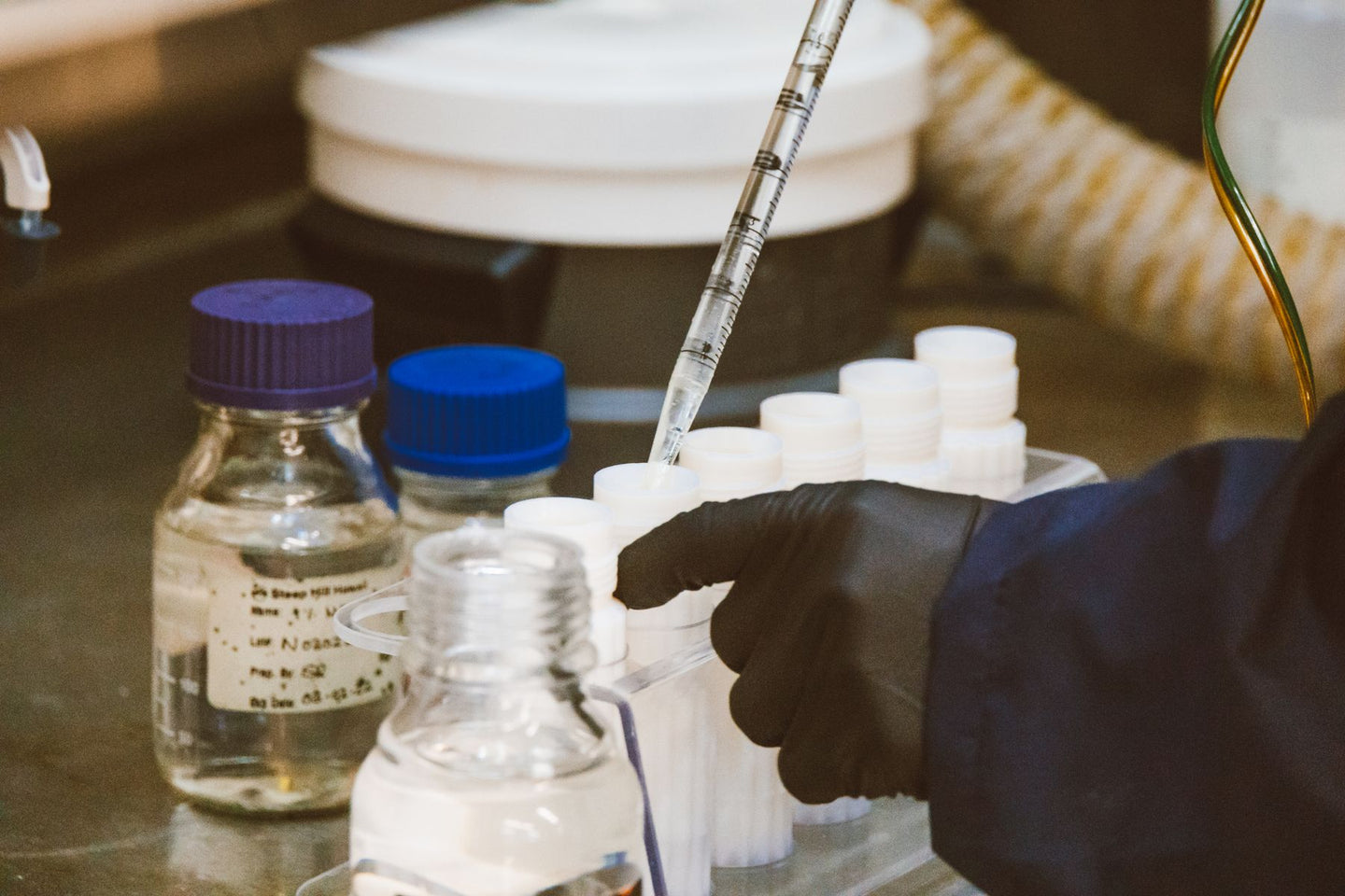 A gloved hand using a glass pipette with laboratory sample tubes