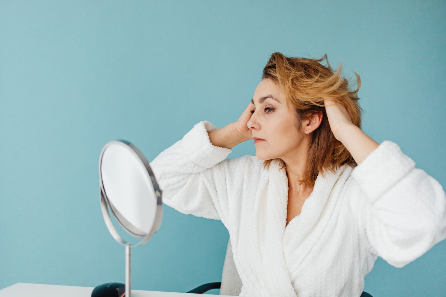 A woman adjusting her hair while looking in a mirror