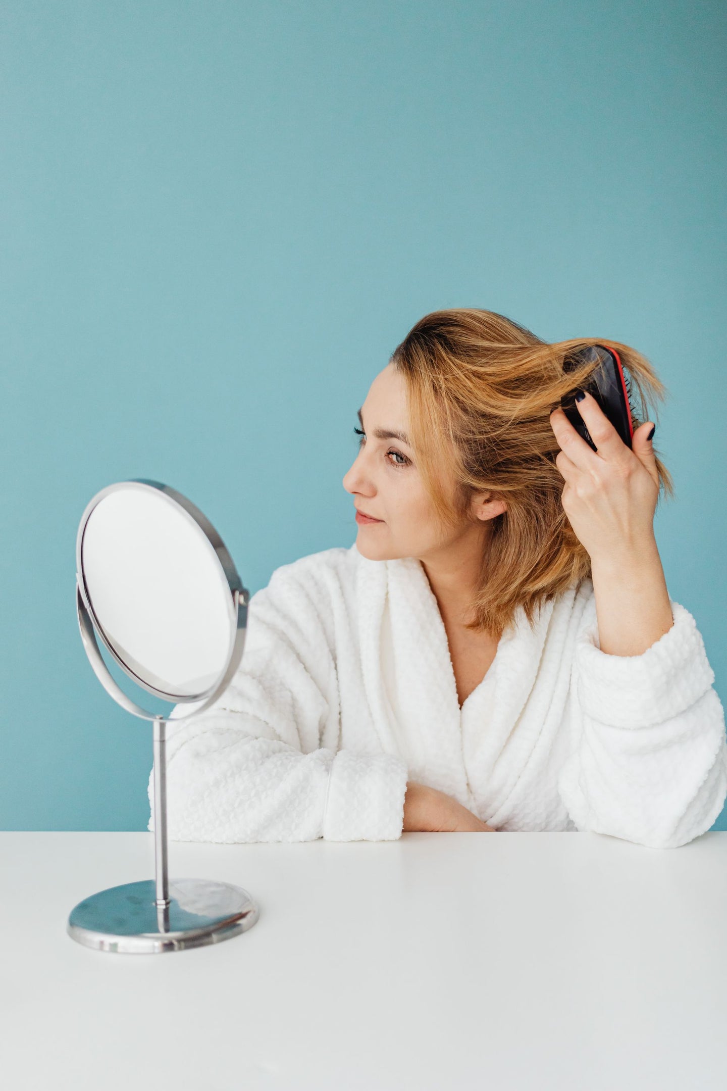 A woman combing her hair while looking in a mirror