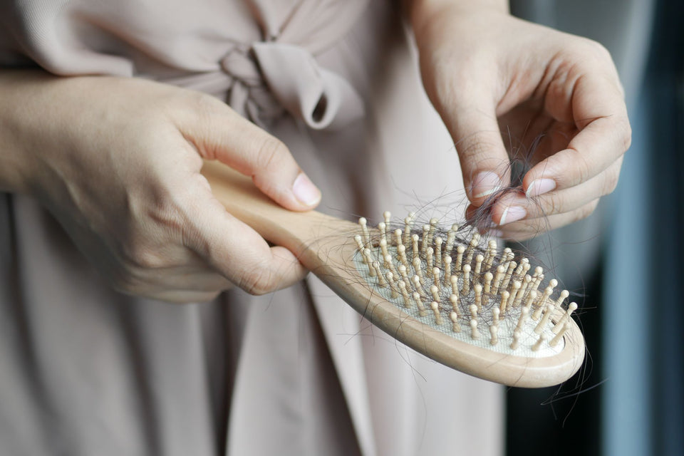 Hands removing loose hair from a wooden hairbrush