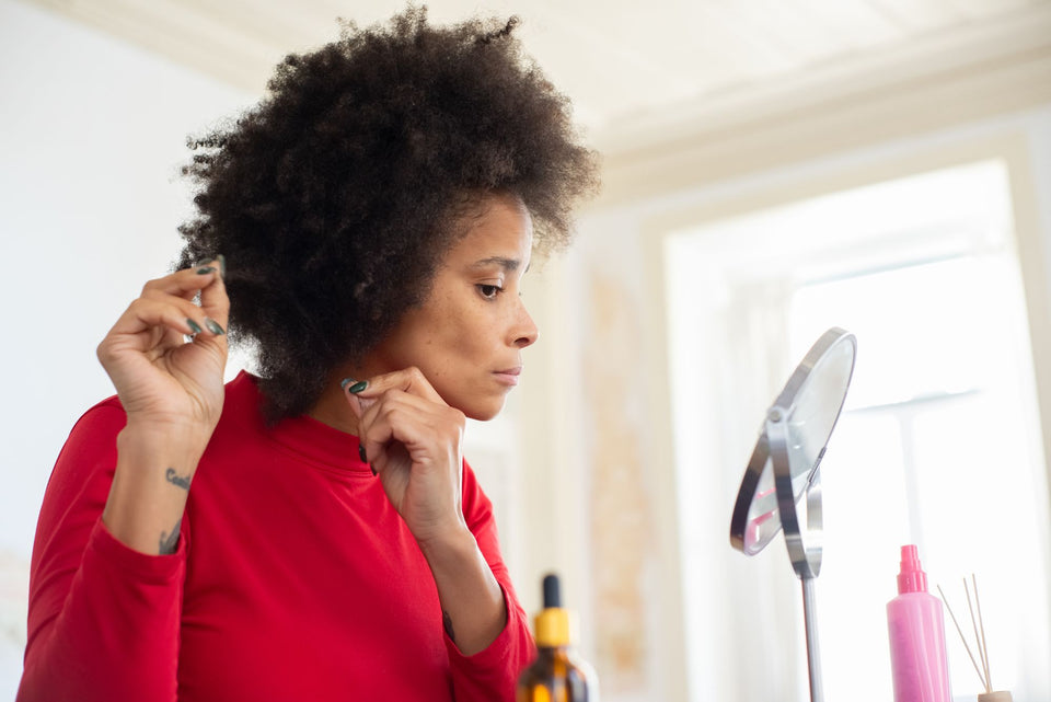 A woman separating her curly hair while looking in a mirror