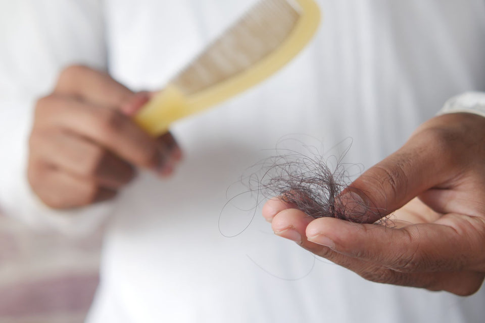 Loose hair strands held in a hand with a brush in the background