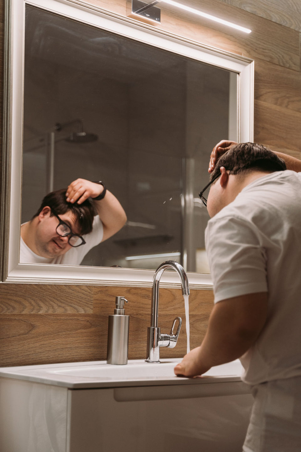 A man checking his hair in a bathroom mirror
