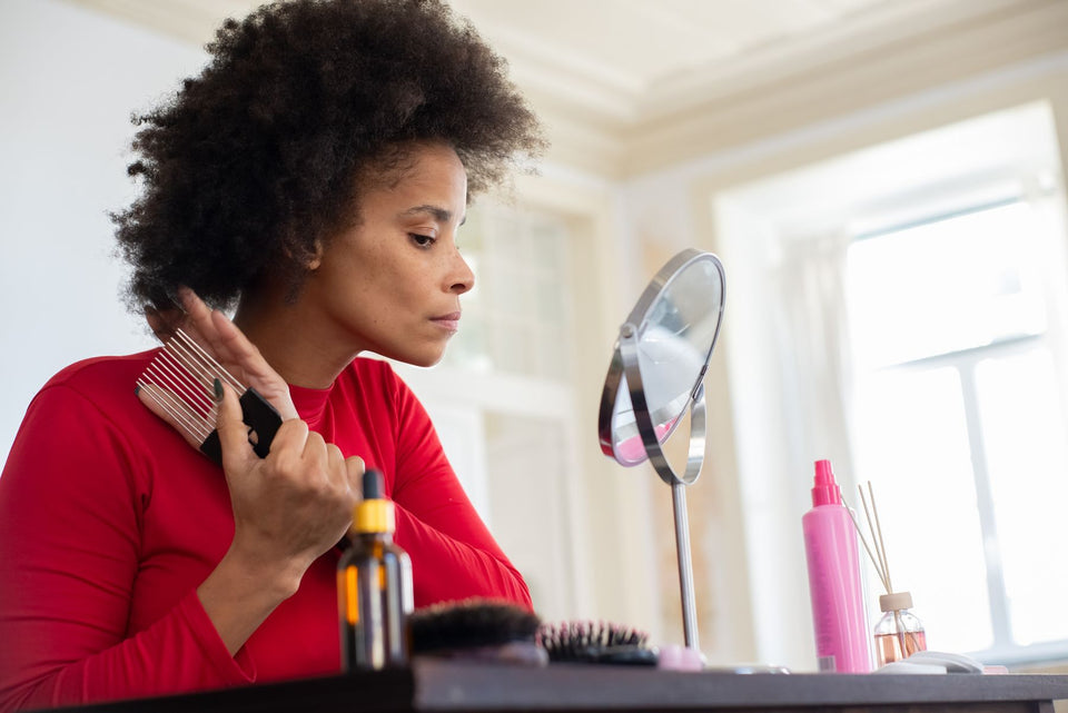 A woman combing her curls while looking in a tabletop mirror