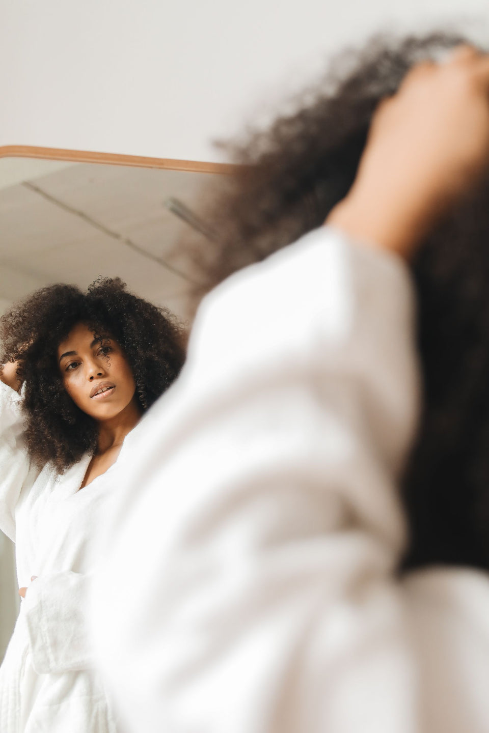 A woman checking her curls in a bathroom mirror