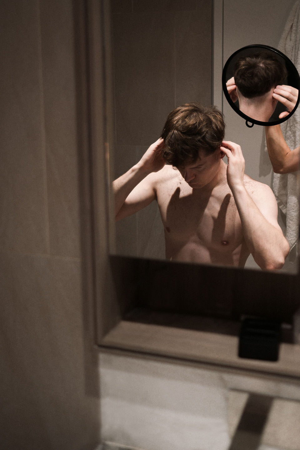 A man checking his hair with a bathroom mirror