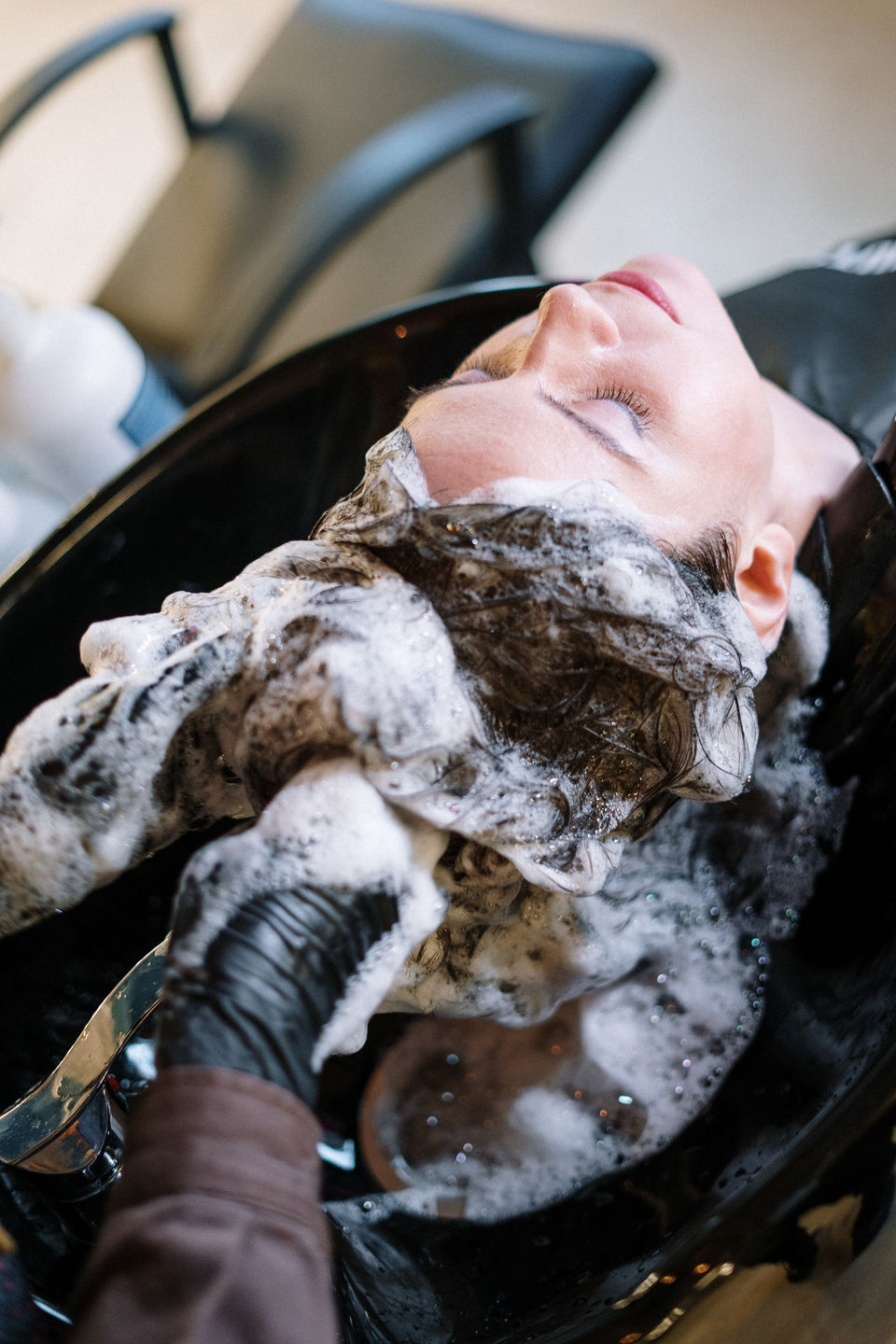 Gloved hands lathering hair at a salon wash basin