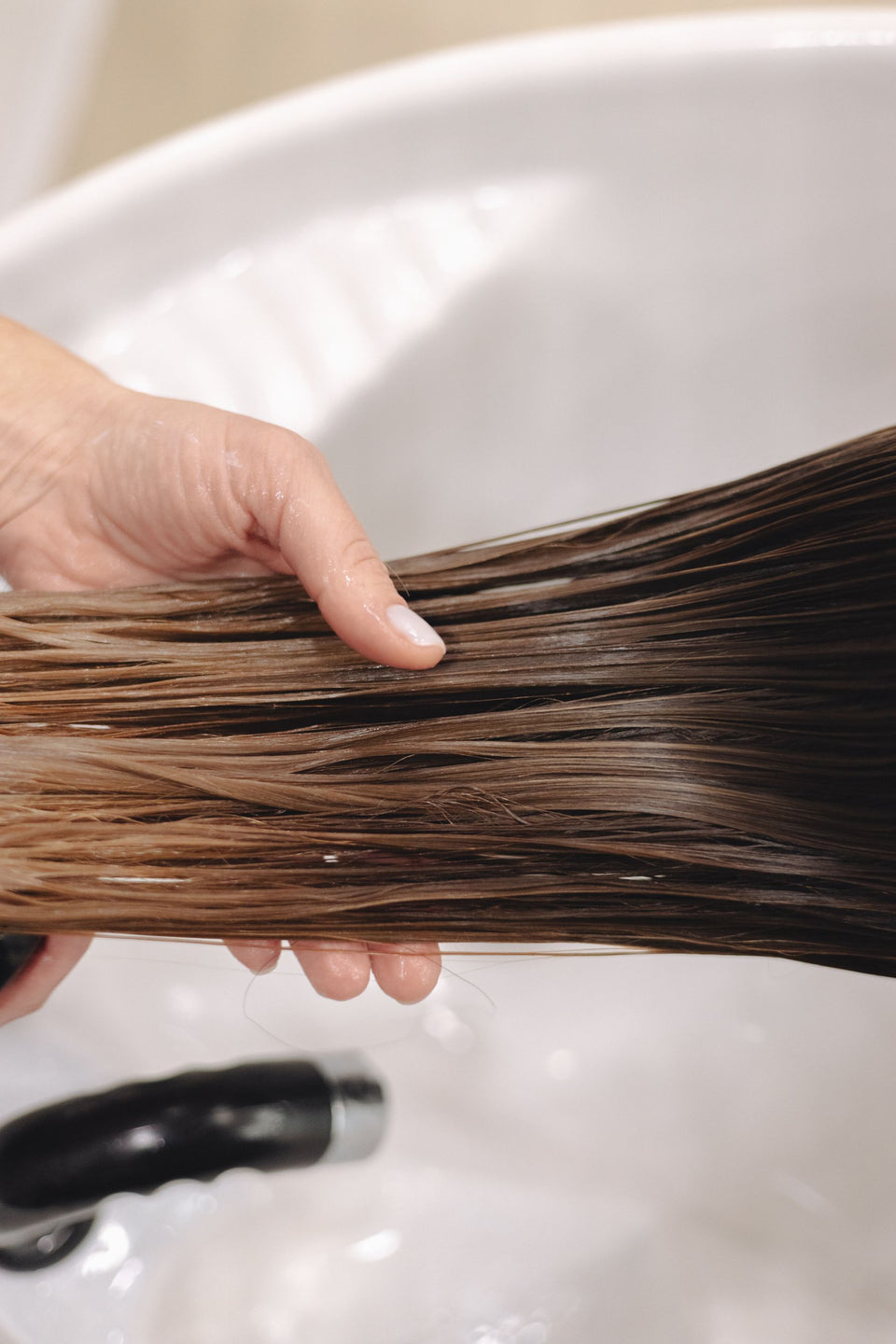 A hand lifting wet hair over a wash basin